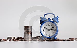 Blue alarm clock and coins. Concepts about budgets and schedules.