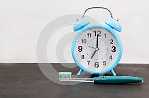 Blue alarm clock and a toothbrush on a black table. The concept of time to brush your teeth. Copy of space. Place for text.