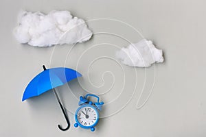 Blue alarm clock under an umbrella on gray background