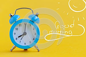 Blue alarm clock on yellow background with text Good morning. Minimalism. Contrast concept