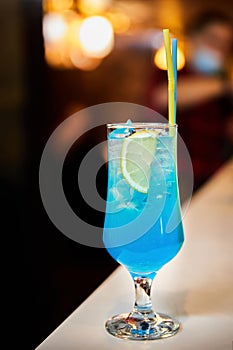 Blue alcoholic cocktail with orange, ice and straw. Close-up, selective focus