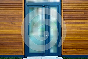 Blue aluminum framed entrance door of a modern office building, walls are tiled with mahogany wood