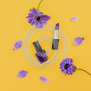 Blue anemones flowers and nail polish and lipstick on yellow background. Flat lay