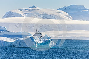 Blue antarctic cruise vessel among the icebergs with glacier in