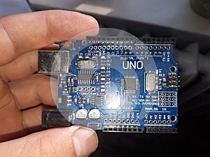 Blue Arduino Uno board electronics in hand for programming the microcontroller