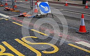 Blue arrow direction sign, next to orange roadworks cones, yellow bus text on asphalt near