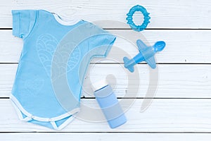 Blue baby clothes for little boy. Bodysuit, toys, cosmetics on white wooden background top view copy space