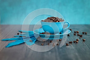 Blue background blue coffee cup sitting on a blue saucer filled with coffee beans