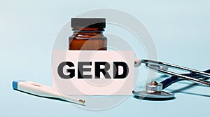 On a blue background - a bottle for pills, a stethoscope, an electronic thermometer and a card with the inscription GERD. Medical