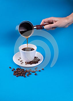 On a blue background a cup with a saucer, grains and a hand pouring coffee