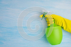 On a blue background, a hand in a yellow glove holds a green bottle for spraying liquids, there is a place for writing on the left