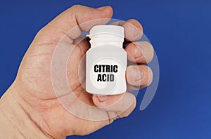 On a blue background in the hands of a man is a white jar with the inscription - Citric Acid