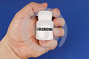 On a blue background in the hands of a man is a white jar with the inscription - Colchicine