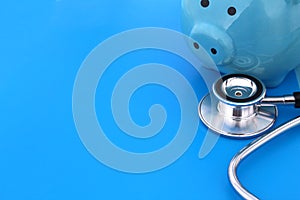 On a blue background lies a stethoscope and a piggy bank.