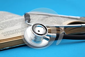 On a blue background lies a textbook book with a stethoscope. Medical education theme.