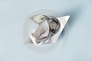 On a blue background, a man in a paper boat holds a hundred-dollar bill like a sail