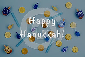 Blue background with multicolor dreidels, menora candles and chocolate coins and Happy Hanukkah wording. Hanukkah and