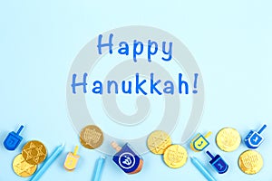 Blue background with multicolor dreidels, menora candles and chocolate coins and Happy Hanukkah wording. Hanukkah and photo