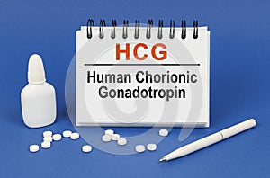 On a blue background, a pen, tablets and a notepad with the inscription - HCG human chorionic gonadotropin