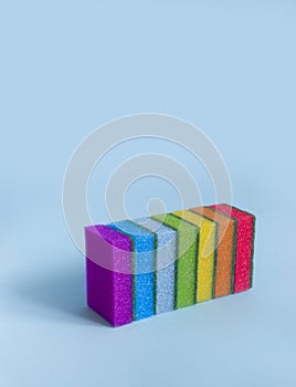 On a blue background are rectangular washcloths in a row of seven sponges for dishes to clean all rainbow colors