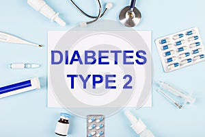 On a blue background, a stethoscope, a thermometer, pills, medicine bottles and a piece of paper with the text DIABETES TYPE 2