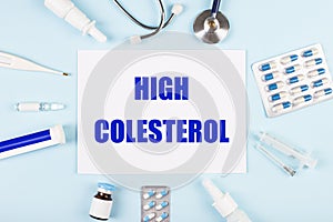 On a blue background, a stethoscope, a thermometer, pills, medicine bottles and a piece of paper with the text HIGH COLESTEROL photo