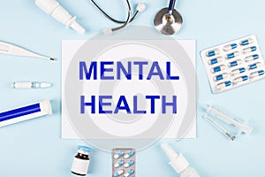 On a blue background, a stethoscope, a thermometer, pills, medicine bottles and a piece of paper with the text MENTAL HEALTH