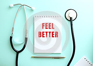 On a blue background, a stethoscope and a white notepad with the red words FEEL BETTER.