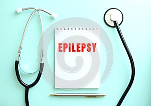 On a blue background, a stethoscope and a white notepad with the words EPILEPSY.
