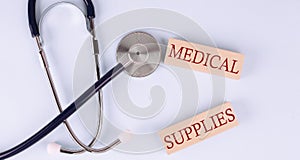 On a blue background, a stethoscope and wooden block with the word MEDICAL SUPPLIES .Medical concept