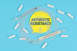 On a blue background, there are pills, a thermometer and a sticker with the inscription ANTIBIOTIC RESISTANCE