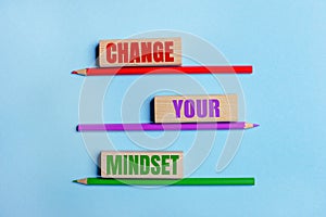 On a blue background, three colored pencils, three wooden blocks with text CHANGE YOUR MINDSET