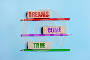 On a blue background, three colored pencils, three wooden blocks with text DREAMS COME TRUE