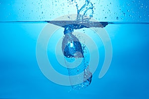 Blue background with water bottle falling in and multiplle drops and splashed. Water bubbles texture