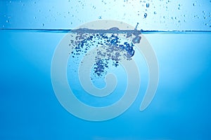 Blue background with water bottle falling in and multiplle drops and splashed. Water bubbles texture