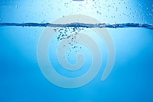 Blue background with water bottle falling in and multiplle drops and splashed. Water bubbles texture