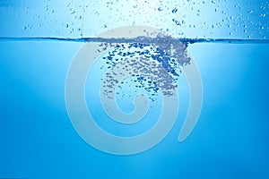 Blue background with water bottle falling in and multiplle drops and splashed. Water bubbles texture