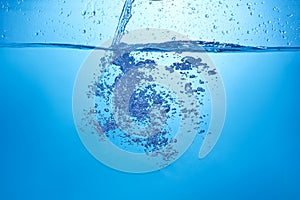 Blue background with water bottle falling in and multiplle drops and splashed. Water bubbles texture