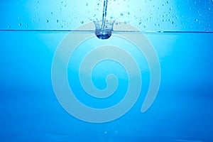 Blue background with water bottle falling in and multiplle drops and splashed. Water bubbles texture
