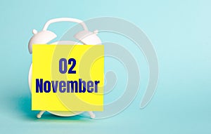 On a blue background - a white alarm clock with a yellow sticker for notes with the text NOVEMBER 02