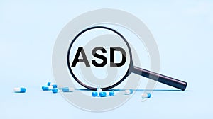 On a blue background, white and blue capsules with pills and a black magnifying glass with the text ASD Autism Spectrum Disorder.