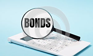 On a blue background, a white calculator and a magnifying glass with the text BONDS. Business concept