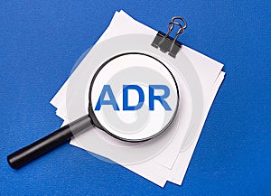 On a blue background, white sheets under a black paper clip and on them a magnifying glass with the text ADR Alternative Dispute