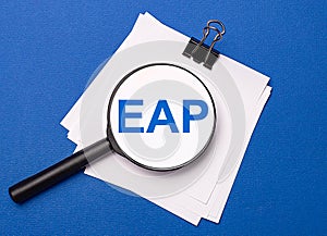On a blue background, white sheets under a black paper clip and on them a magnifying glass with the text EAP Employee Assistance