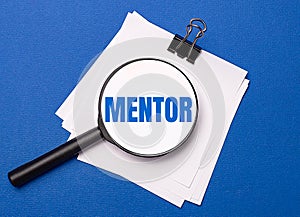 On a blue background, white sheets under a black paper clip and on them a magnifying glass with the text MENTOR