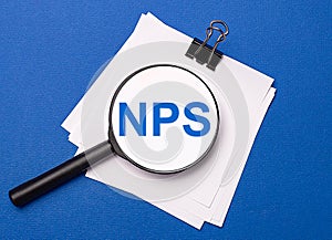 On a blue background, white sheets under a black paper clip and on them a magnifying glass with the text NPS Net Promoter Score