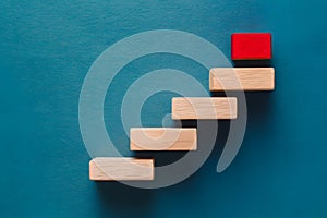 Blue background with wooden staircase culminating in red block, symbolizing progress and achievement in structure photo