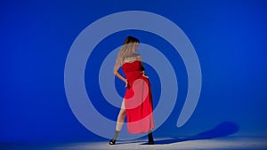 On a blue background. Young woman, showing dance moves towards high heels. A spotlight beam shines on her and gives her