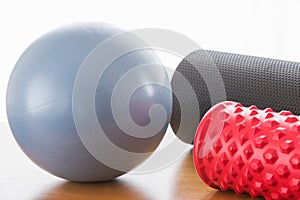 A blue ball and a grey pilates roller and a red fascial massage roller