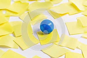 A blue ball perched atop a stack of yellow post-it notes, ideal for use in illustrations or designs about creativity